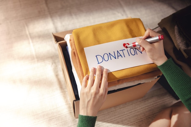 Concepto de donación de ropa. Caja de Paño con etiqueta Donar. Mujer preparando ropa vieja usada en casa. Vista superior