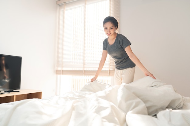 Concepto de dormitorio una mujer adulta que hace la rutina agarrando el borde de la manta para hacer la cama después de levantarse por la mañana.