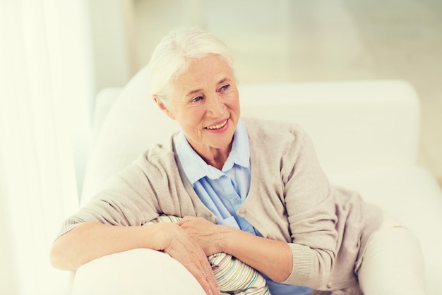 concepto de edad y personas - anciana sonriente feliz sentada en un sofá en casa