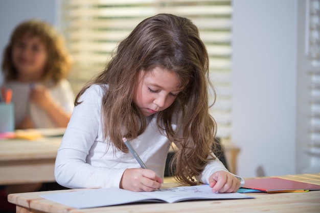 Concepto de educación, aprendizaje y niños. Alumno de niña estudiante con prueba de escuela de escritura de libros. De vuelta a la escuela. Niño lindo feliz está sentado en un escritorio en el interior. El niño está aprendiendo en clase.