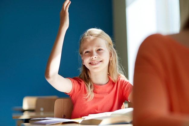 concepto de educación, aprendizaje y personas - niña estudiante feliz levantando la mano en la lección de la escuela