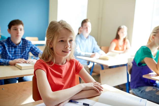 concepto de educación, aprendizaje y personas - niña estudiante feliz con libro en la lección de la escuela