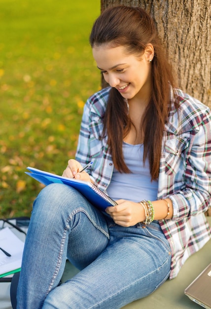 concepto de educación, campus y personas - adolescente sonriente escribiendo en un cuaderno