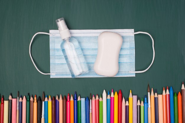 Concepto de educación en casa. Arriba arriba foto de vista aérea de jabón desinfectante de mascarilla y lápices y marcadores multicolores aislados en greenboard