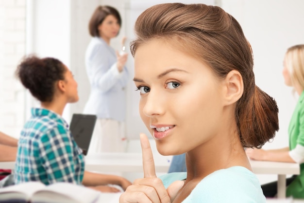 Concepto de educación - chica estudiante haciendo gesto de silencio en la escuela