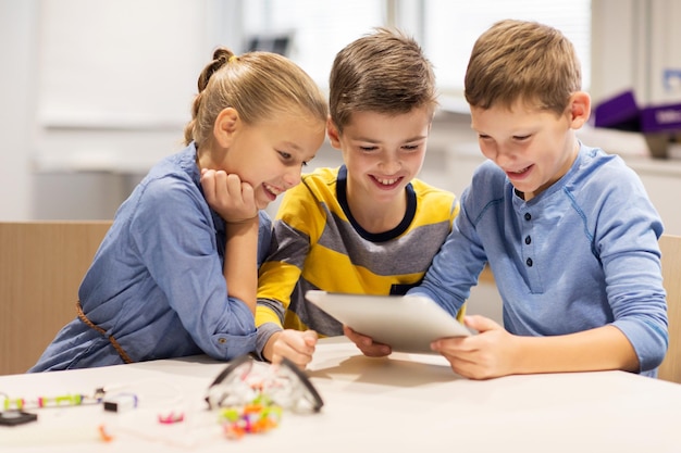 concepto de educación, ciencia, tecnología, niños y personas - grupo de niños felices o estudiantes con tablet pc programando juguetes eléctricos y construyendo robots en la lección de la escuela de robótica