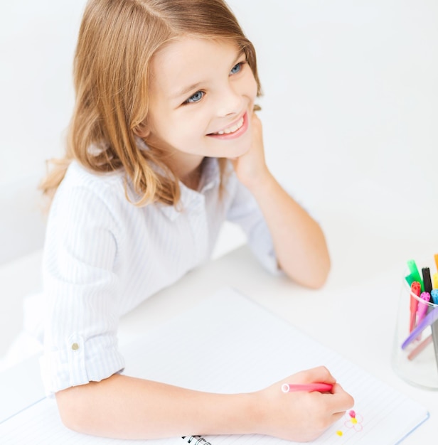 concepto de educación, creación y escuela - sonriente niña estudiante dibujando y soñando despierto en la escuela