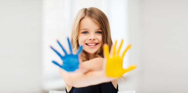 concepto de educación, escuela, arte y pintura - niña estudiante mostrando las manos pintadas en la escuela