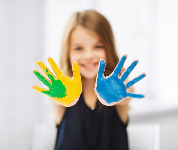 concepto de educación, escuela, arte y pintura - niña estudiante mostrando las manos pintadas