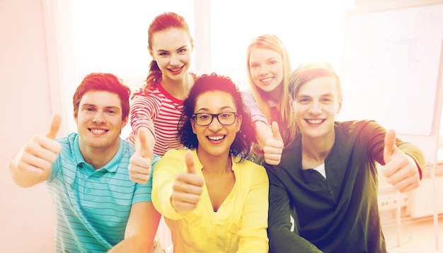 concepto de educación y escuela - grupo de estudiantes sonrientes en la escuela mostrando los pulgares hacia arriba