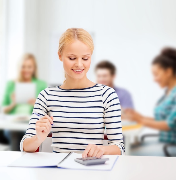 concepto de educación, escuela y negocios - mujer sonriente con cuaderno y calculadora estudiando en la universidad