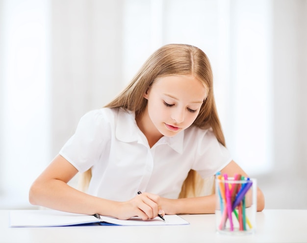 Concepto de educación y escuela - niña estudiante dibujando en la escuela