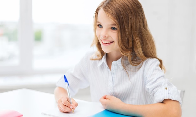 Concepto de educación y escuela - niña estudiante escribiendo en el cuaderno en la escuela