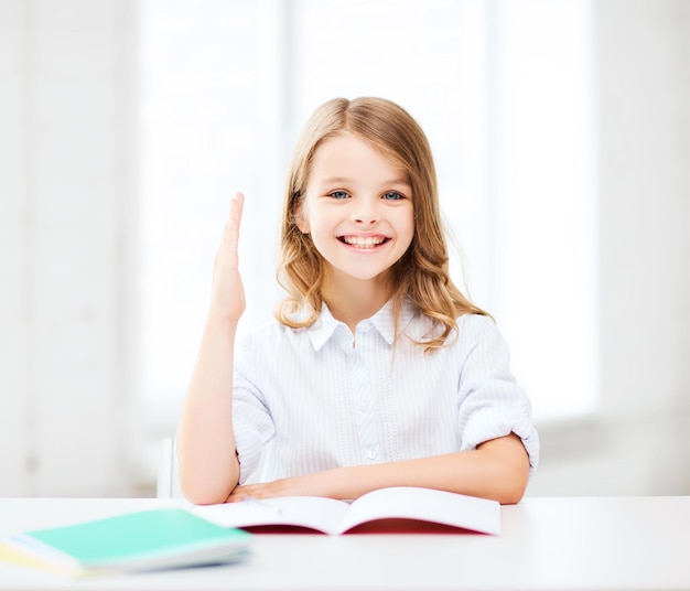 Concepto de educación y escuela - niña estudiante estudiando y levantando la mano en la escuela