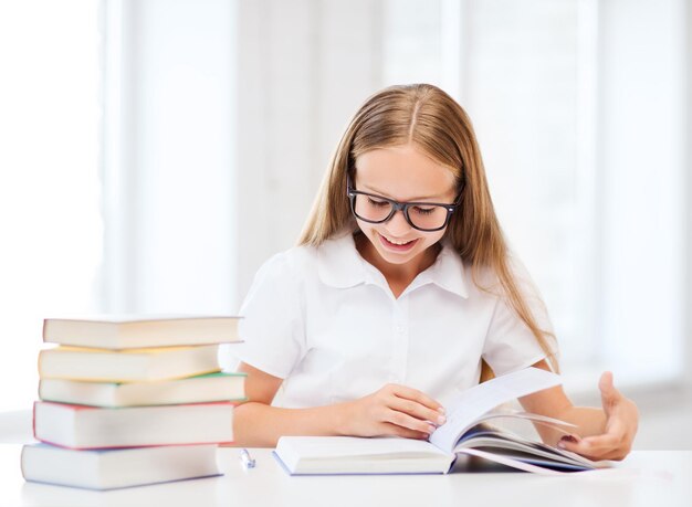 Concepto de educación y escuela - niña estudiante estudiando y leyendo libros en la escuela