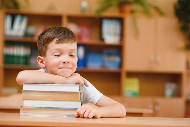 Concepto de educación y escuela - niño sonriente con muchos libros en la escuela