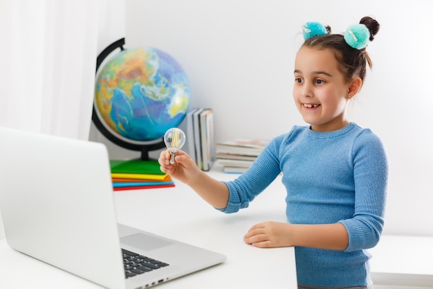 concepto de educación, escuela, tecnología e internet - niña estudiante apuntando a la computadora portátil con bombillas en la escuela