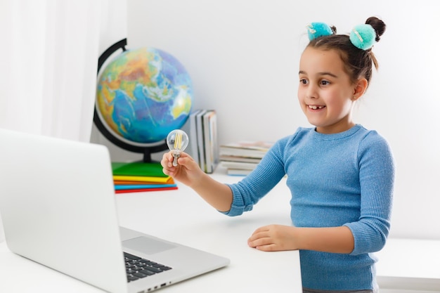 concepto de educación, escuela, tecnología e internet - niña estudiante apuntando a la computadora portátil con bombillas en la escuela