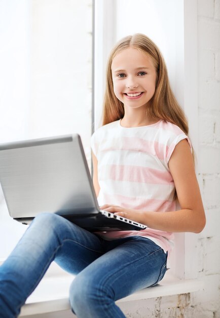 Concepto de educación, escuela, tecnología e internet - niña estudiante con computadora portátil en la escuela