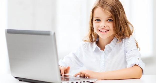 Concepto de educación, escuela, tecnología e internet - niña estudiante con computadora portátil en la escuela