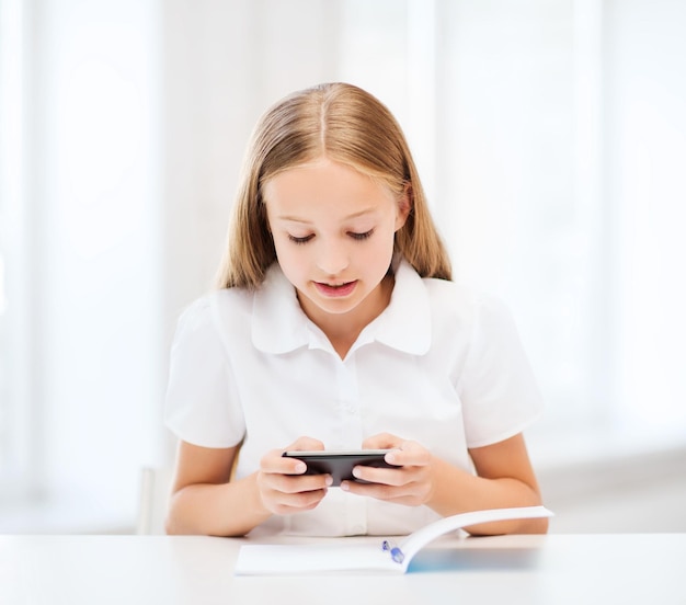 concepto de educación, escuela, tecnología e internet - niña estudiante con teléfono inteligente en la escuela