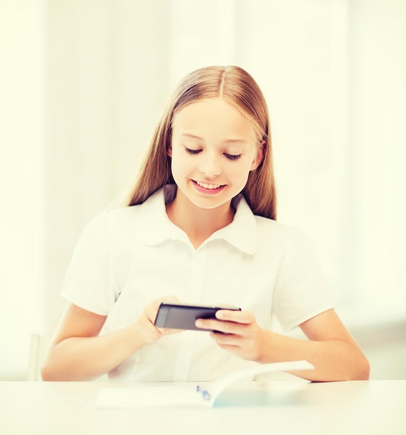 concepto de educación, escuela, tecnología e internet - niña estudiante con teléfono inteligente en la escuela