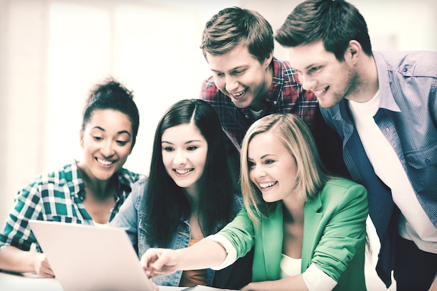 concepto de educación - estudiantes sonrientes mirando portátil en la escuela