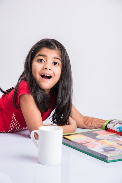 Concepto de educación en el hogar: linda niña india o asiática que estudia con una pila de libros y una taza de café mientras está sentado en el suelo en casa. Aislado sobre fondo blanco