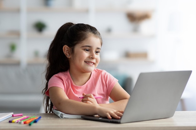 Concepto de educación en el hogar Linda niña preadolescente usando una computadora portátil para estudiar en línea en casa