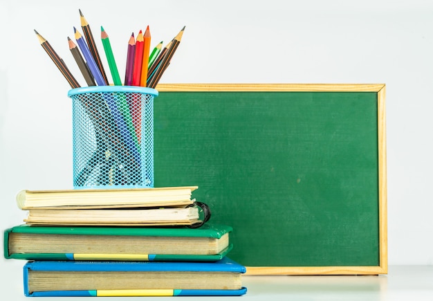 Concepto de educación Lápices de colores en portalápices y libros sobre mesa blanca