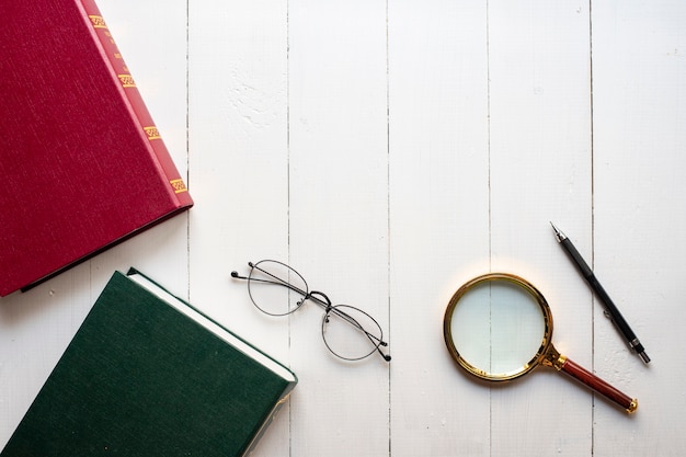 Concepto de educación, libro, pluma, lentes, lupa sobre fondo blanco de madera