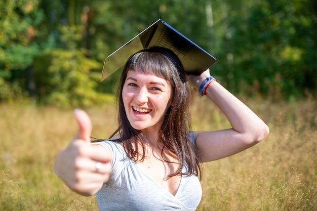 Concepto de educación en línea niña estudiante sostiene una computadora portátil sobre su cabeza como una gorra académica cuadrada y