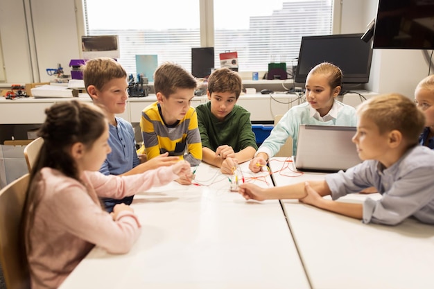 concepto de educación, niños, tecnología, ciencia y personas - grupo de niños felices con juegos de computadora portátil y kit de invención en la lección de la escuela de robótica