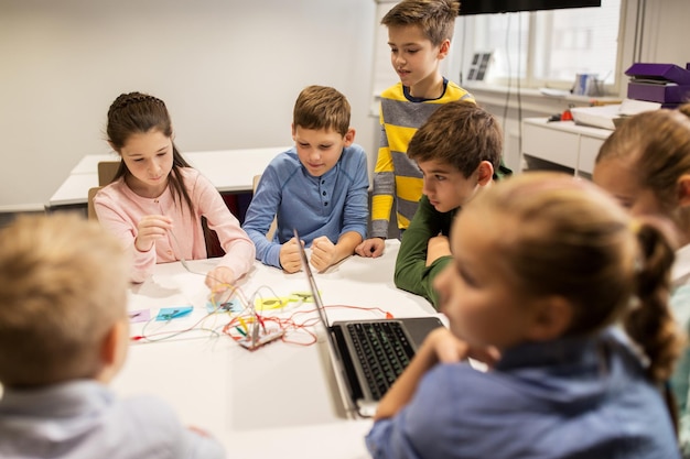 concepto de educación, niños, tecnología, ciencia y personas - grupo de niños felices con juegos de computadora portátil y kit de invención en la lección de la escuela de robótica