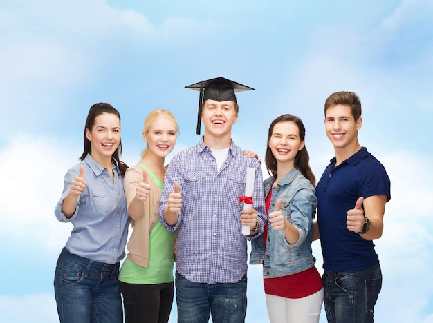 Concepto de educación y personas - grupo de estudiantes sonrientes de pie con diploma y tapa de esquina mostrando los pulgares para arriba