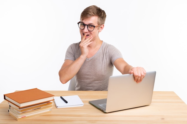 Concepto de educación y personas - hombre divertido estudiante sentado en la mesa de madera con ordenador portátil y libros