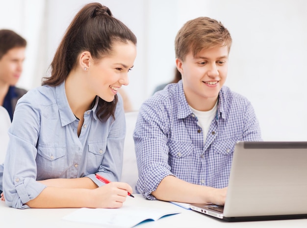 Concepto de educación, tecnología e internet: dos estudiantes sonrientes con computadora portátil y cuadernos en la escuela