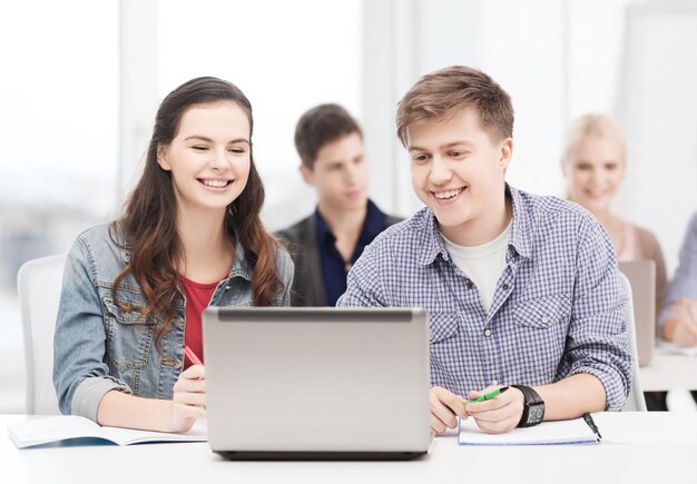 Concepto de educación, tecnología e internet: dos estudiantes sonrientes con computadora portátil y cuadernos en la escuela