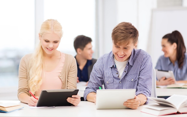 concepto de educación, tecnología e internet - dos estudiantes sonrientes con tablet pc, cuadernos y libros en la escuela