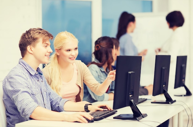 Concepto de educación, tecnología e internet - grupo de estudiantes sonrientes con monitor de computadora mirando al maestro en la escuela