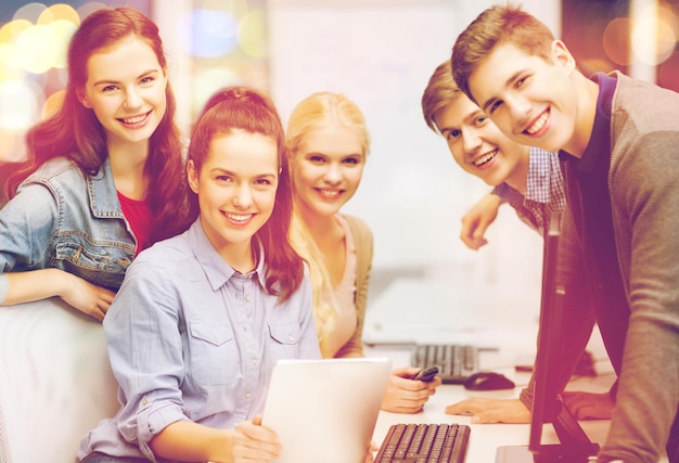 Concepto de educación, tecnología e internet - grupo de estudiantes sonrientes con monitor de computadora y tablet pc