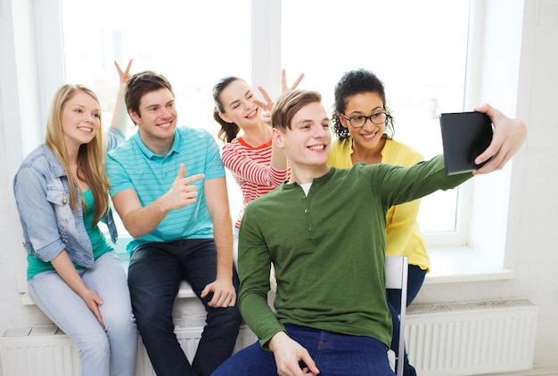 concepto de educación y tecnología - estudiantes sonrientes haciendo fotos con una tableta en la escuela