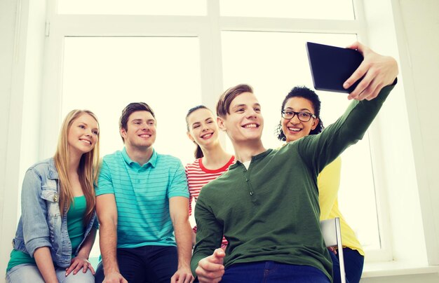 concepto de educación y tecnología - estudiantes sonrientes haciendo fotos con una tableta en la escuela