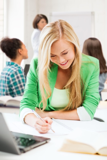 Concepto de educación y tecnología - niña estudiante sonriente escribiendo en el cuaderno en la escuela