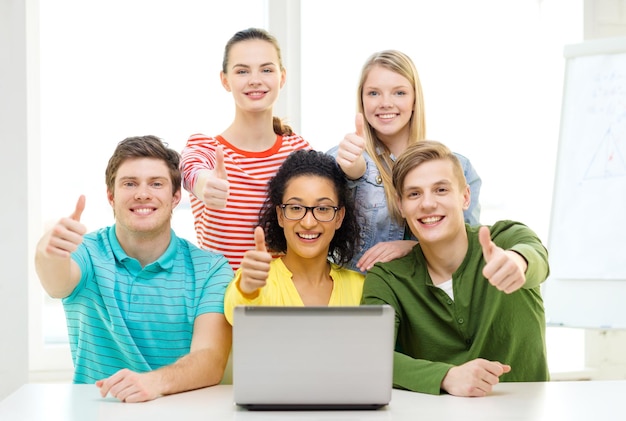 concepto de educación y universidad - cinco estudiantes sonrientes con laptop en la escuela mostrando los pulgares hacia arriba