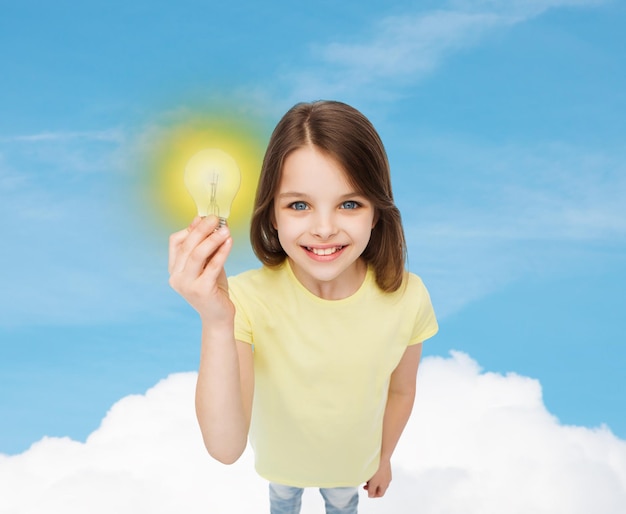 concepto de electricidad, educación y personas - niña sonriente sosteniendo una bombilla