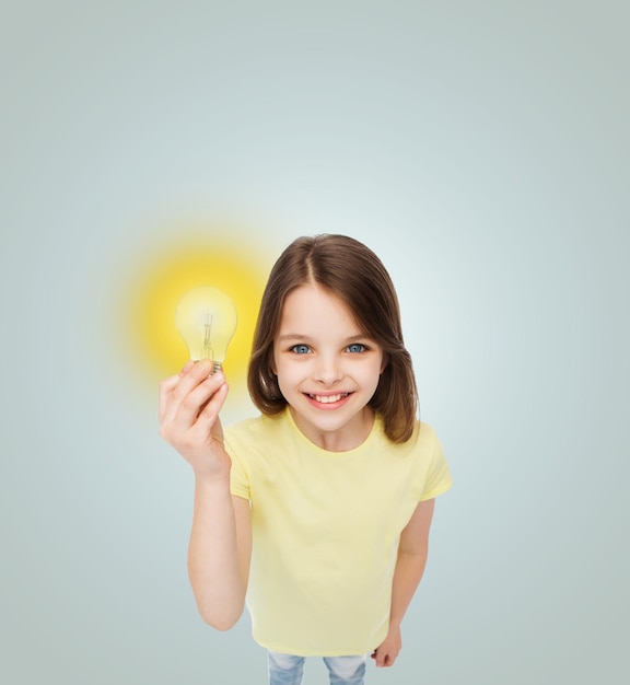 concepto de electricidad, educación y personas - niña sonriente sosteniendo una bombilla