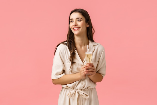 Concepto de elegancia, romance y ternura. Encantadora mujer morena bonita en vestido encantador contemplando la hermosa ceremonia de boda, siendo una fiesta de invitados, sosteniendo una copa de champán y sonriendo