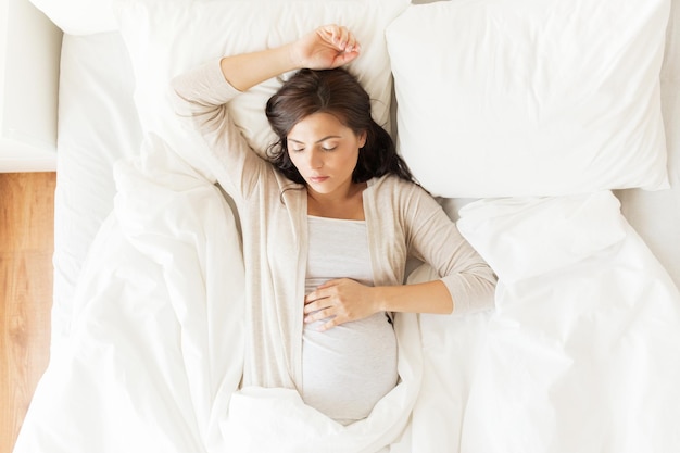 concepto de embarazo, descanso, personas y expectativas - mujer embarazada feliz durmiendo en la cama en casa