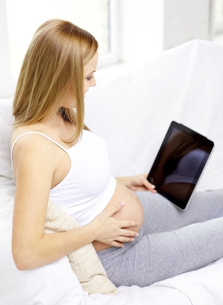 concepto de embarazo, maternidad, tecnología, personas y expectativas: cerca de una mujer embarazada feliz con una tableta en casa